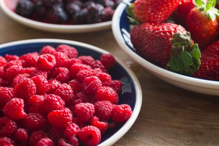 Blue plate full of juicy,delicious, healthy raspberries. Shallow depth of field, strawberries and blackberries in the background.の写真素材