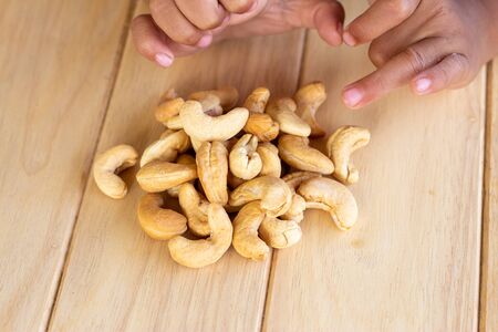 Many Roasted salted cashew nuts  and kid hand on wooden backgroundの写真素材