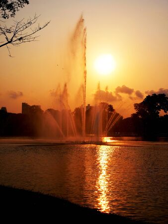 A fountain jets water high into the sky with rising sun as a background.の写真素材