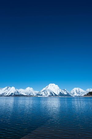 The tranquility of a blue lake with snowy  mountains. This picture was taken from a lake in Grand Teton National Park , United States in May 2017.の写真素材