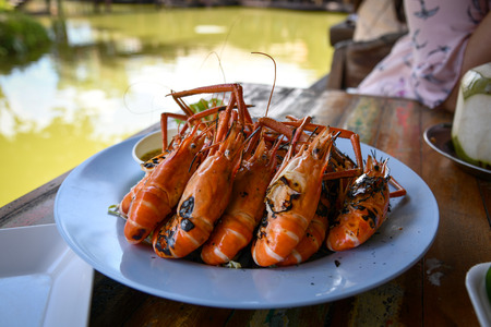 Grilled shrimps serve with thai spicy seafood sauce on blue plate on wooden table at riverside restaurant in Ayutthaya province, Thailand.の写真素材