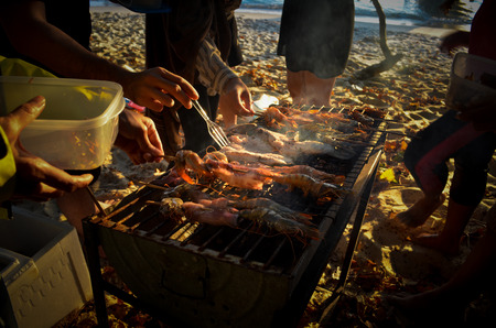 Group of people helping each other to make delicious dinner before sunset at the beach in Thailand which is grilled seafood with thai spicy sauce.の写真素材