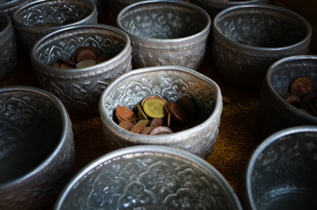 Golden, bronze and silver Thai coins separated in silver bowls for thai traditional donation at...