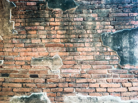 An aged, cracked and chipped stucco wall with an area of exposed brown brick. Brick wall background texture.の写真素材