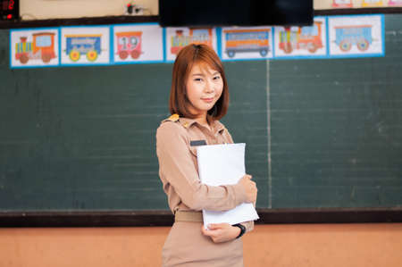 Female thai teacher in uniform standing in front of the classroom wearing mask and greeting with green virus around herの写真素材