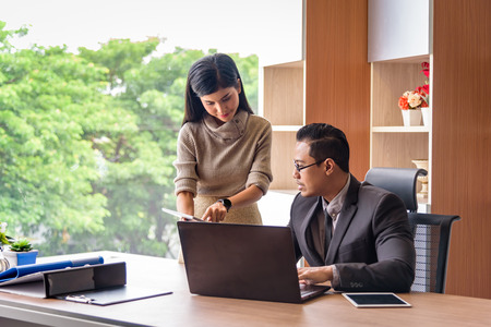 asian beautiful secretary helping boss, showing information from tablet, in office の写真素材