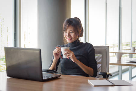 young asian businesswoman working while holding white cup coffee in the officeの写真素材