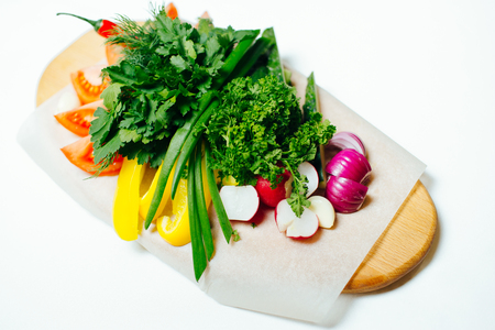Fresh isolated vegetables on a wooden board on a white background consisting of radishes, green onions, parsley, tomato, pepper ringsの写真素材
