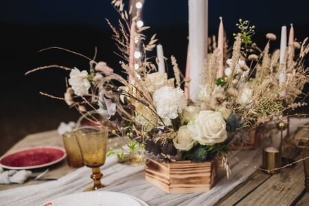 Romantic dinner of the bride and groom on a wooden table with burgundy plates and fresh flowers.