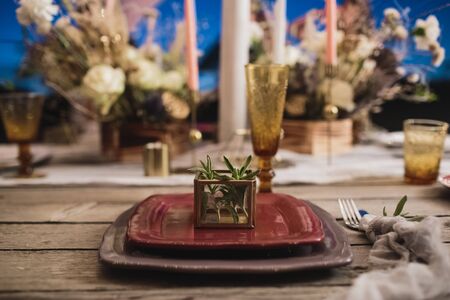 Romantic dinner of the bride and groom on a wooden table with burgundy plates and fresh flowers.の写真素材