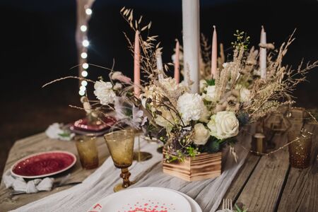 Romantic dinner on a wooden table with burgundy plates and fresh flowers.の写真素材