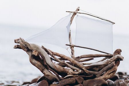 Decorative ship made of branches and roots with a sail on the seashore.の写真素材