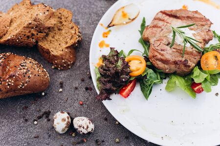 Grilled steak and vegetables on a dish with brown bread.