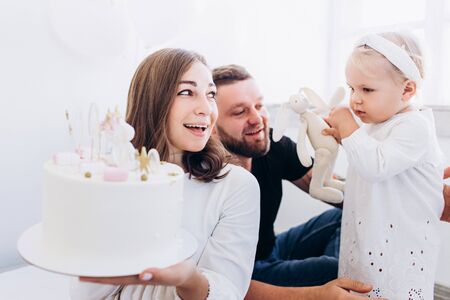 Family is playing with a little daughter. Child in a white dress with dad and mom. Happy birthday.の写真素材
