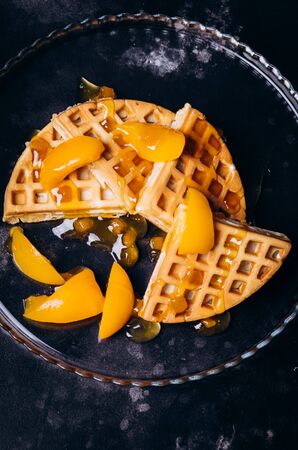 Waffles with peaches for breakfast on a black background. Traditional morning breakfast.の写真素材