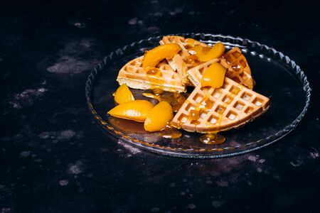 Waffles with peaches for breakfast on a black background. Traditional morning breakfast.の写真素材