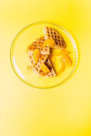 Waffles with peaches for breakfast on a yellow background. Traditional morning breakfast.の写真素材