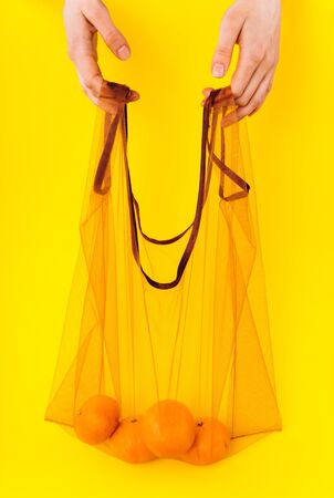 Eco package with tangerines on a bright yellow background. Zero waste and anti-plastic bag.の写真素材