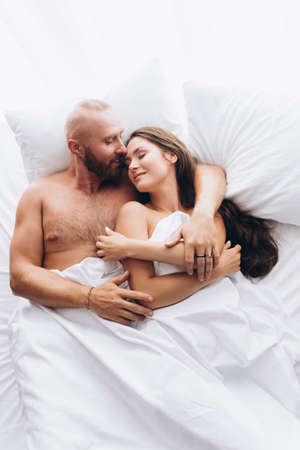 Loving couple in bed on white sheets. Stay at home.の写真素材