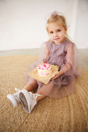 Little white Birthday girl with cake in a pink dress laughs. Preschooler.の写真素材