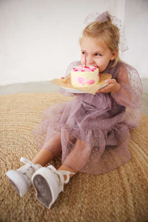 Little white Birthday girl with cake in a pink dress laughs. Preschooler.の写真素材