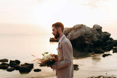 Groom with a wedding bouquet on the beach. Groom in boho style.の写真素材