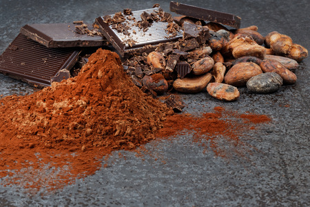 Chocolate pieces with cocoa beans and cocoa powder on a stone tableの写真素材