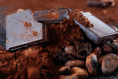 Chocolate pieces with cocoa beans and cocoa powder on a stone tableの写真素材