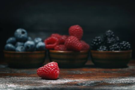 Blueberries, blackberries and raspberries in bowls on a wooden table