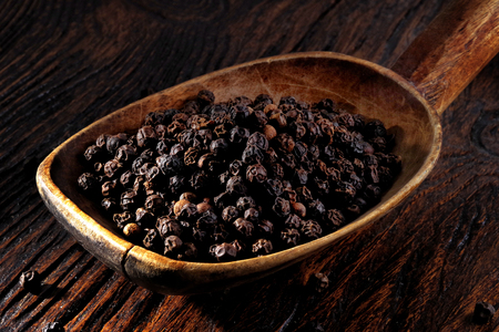 Black pepper in wooden spoon on wooden tableの写真素材