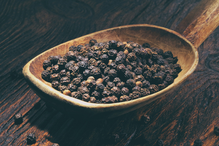 Black pepper in wooden spoon on wooden table