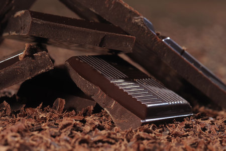 Broken dark chocolate bar and chocolate flakes on black kitchen tableの写真素材