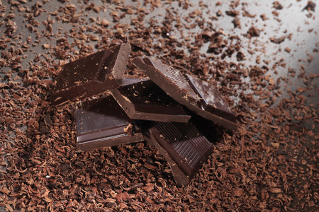 Broken dark chocolate bar and chocolate flakes on black kitchen table