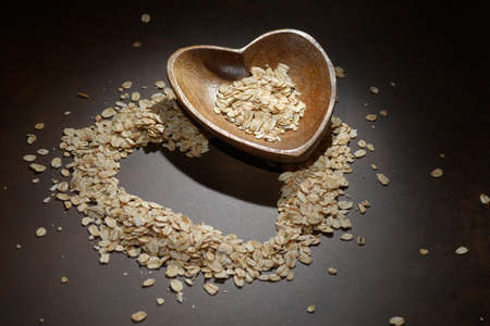 Heap of oat flakes in a shape of heart. Oatmeal heart on a dark background. Healthy eating