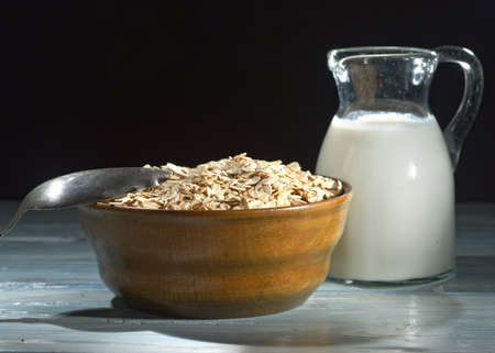 Oatmeal in a wooden bowl, oatmeal and cup of milk on the table. Healthy eatingの写真素材