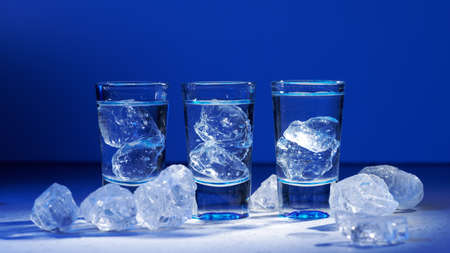Glass of vodka with ice on blue background, selective focusの写真素材