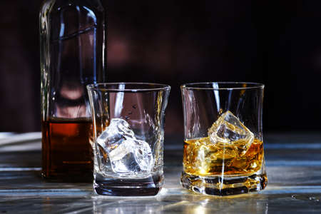 Glass of amber scotch whiskey and ice on a dark background