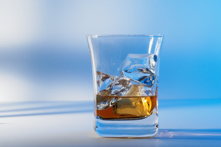 Glass of amber scotch whiskey and ice on a blue backgroundの写真素材