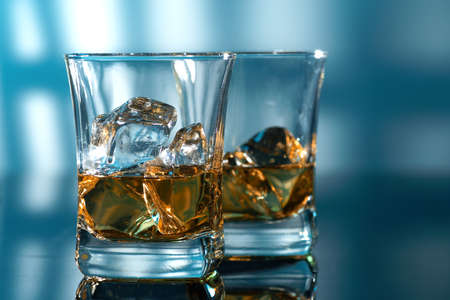 Glass of amber scotch whiskey and ice on a blue backgroundの写真素材
