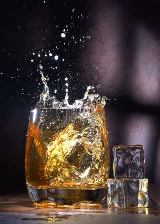 Glass of old whiskey with ice. A splashing glass of whiskey with ice isolated on a dark backgroundの写真素材