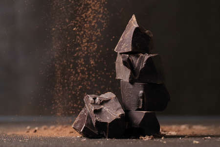 Broken dark chocolate and cocoa powder on a tableの写真素材