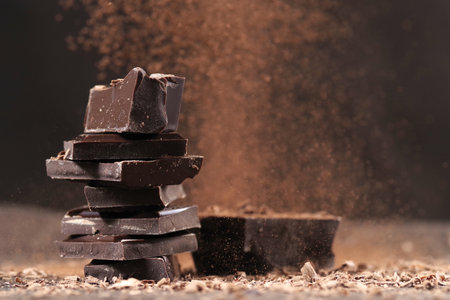 Pieces of dark chocolate with cocoa powder on wooden table, closeup