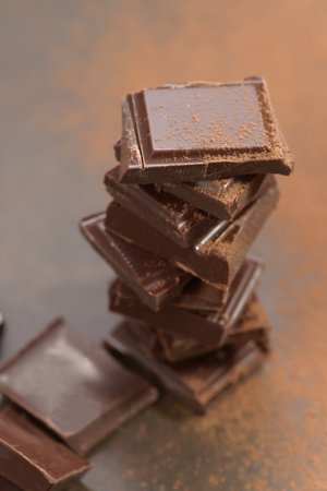 Pieces of dark chocolate stacked on top of each other on a brown backgroundの写真素材