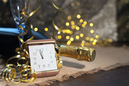 Alarm clock and champagne bottle on table in front of Christmas lights