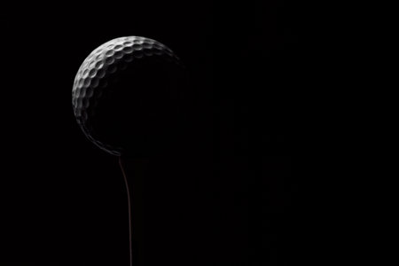 Golf ball on a tee on a dark background close-upの写真素材