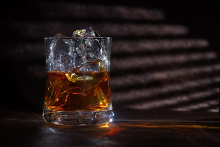 Glass of whiskey with ice cubes on a dark background. Copy space.