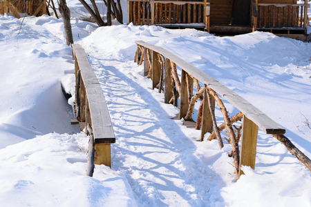 Beautiful wooden bridge from cedar across the river on a sunny winter day. In the villageの写真素材