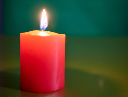 Red wax festive romantic burning candle on a green decorative background. love symbol. festive . romantic dinner.の写真素材