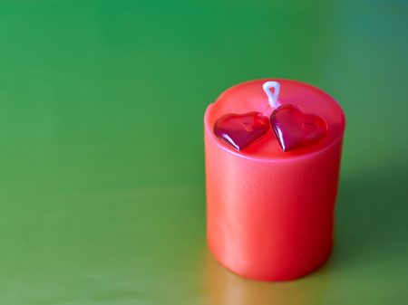 Red wax festive romantic candle on a green decorative background and two red glass hearts lying on a candle. love symbol. festive mood. romantic dinner.の写真素材