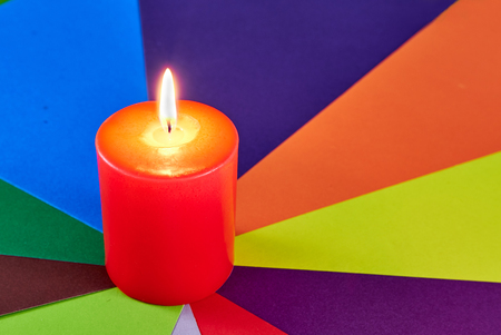Red wax festive romantic burning candle on a multi-colored background from a color juicy cardboard. love symbol. festive mood. romantic dinner.の写真素材